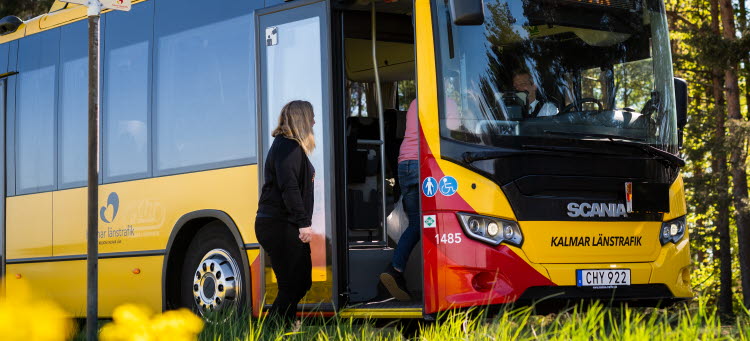 Två personer går ombord via framdörren på en buss vid en hållplats