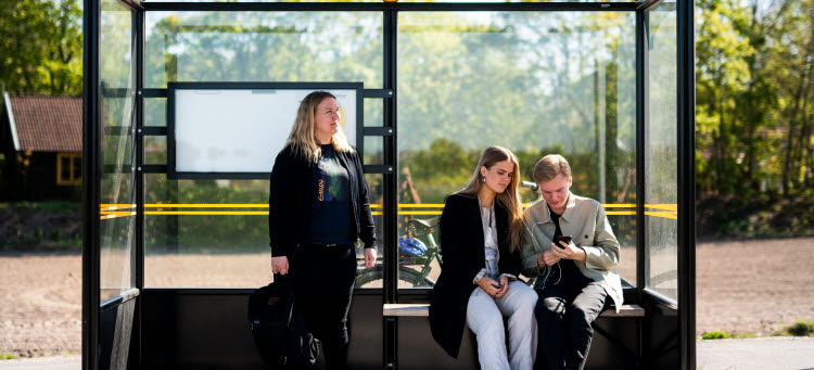 3 personer som väntar på bussen vid en hållplats