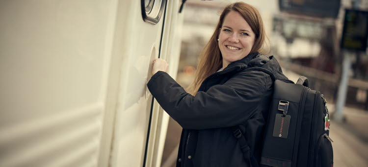 Kvinna står vid en tågdörr och ser glad ut. 