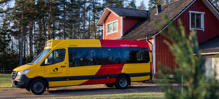 Gul och röd KLT buss som hämtar vid ett rött hus. 